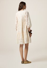 Vestido blanco de eyelet con mangas abullonadas, diseño en capas y recortes florales. Combinado con bailarinas beige que presentan un detalle de hebilla.