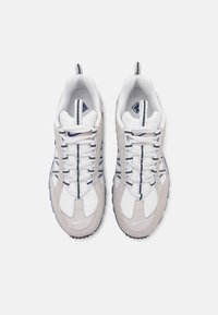 Tênis atléticos brancos e cinzas com materiais em malha e camurça, design com atacadores, detalhes em azul contrastante e solas de borracha texturizadas.