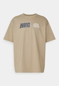 Camiseta de manga corta beige de algodón, con el logo "NBA" y el texto completo "ASOCIACIÓN NACIONAL DE BALONCESTO" en colores oscuros contrastantes.