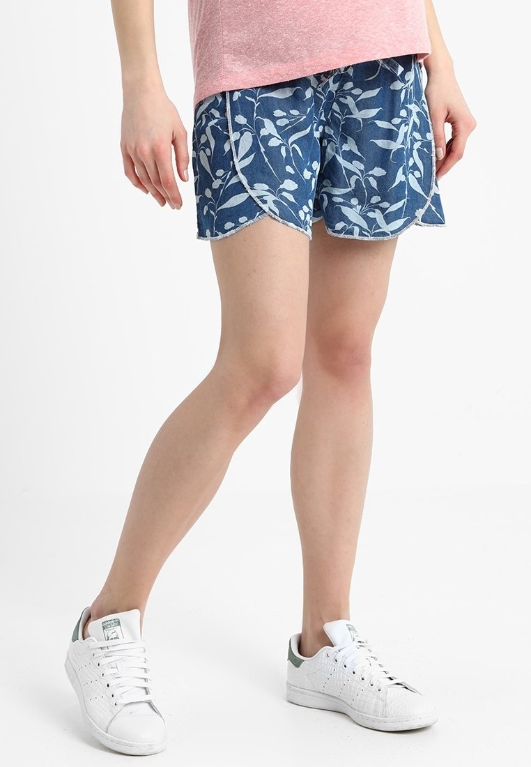 Jeansshorts med blommönster i blått och vitt, med en vågad fåll. Kombineras med vita sneakers och en rosa topp med kort ärm.