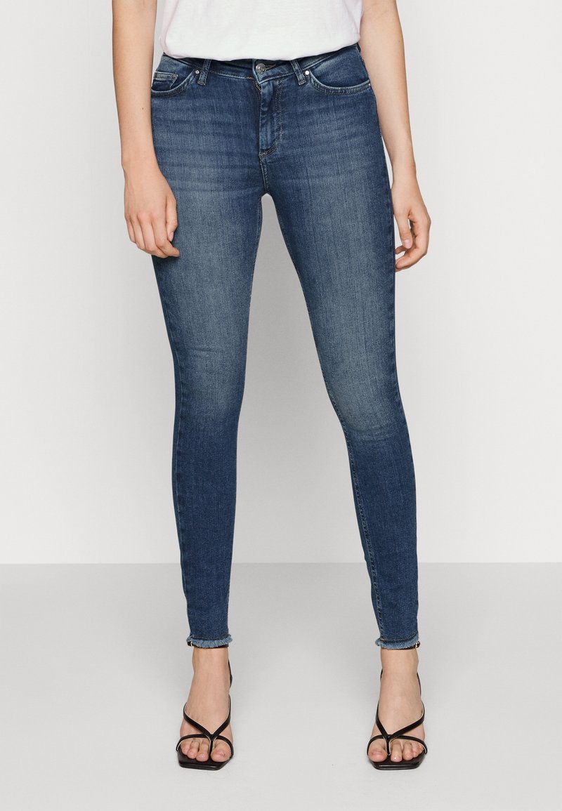 Jean skinny bleu foncé en denim, doté d'un design classique à cinq poches, d'un léger effet délavé et d'ouvertures latérales à l'ourlet.