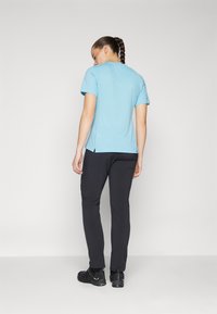 T-shirt de mangas curtas em azul claro com um corte descontraído, combinado com calças pretas ajustadas e calçado preto, apresentando fendas laterais subtis.