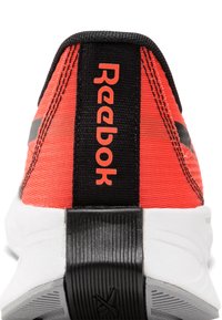 Baskets Reebok avec un dessus en textile rouge et des accents noirs, un talon rembourré et une semelle texturée blanche et noire. Logo affiché sur le talon.