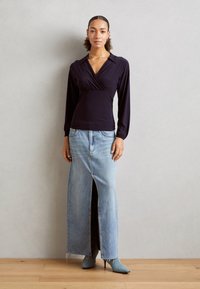 Langermet, dyp marineblå omslagstopp paret med en lyseblå denim maxiskjørt med frontspalte og frynset kant, komplementert av spisse støvler.