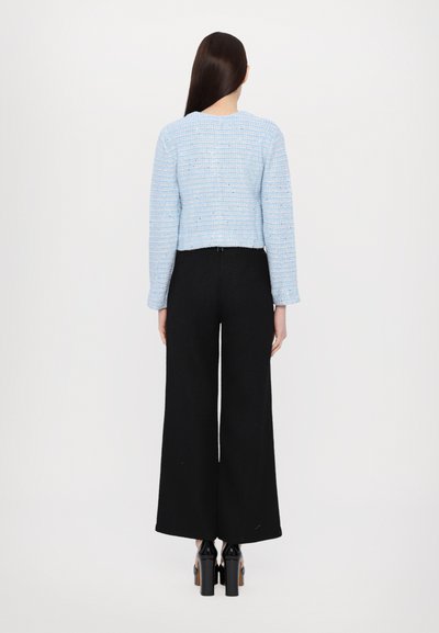Blue textured cropped jacket with long sleeves, paired with black wide-leg pants. Includes a rounded neckline and sleek black shoes.