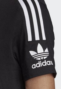 Čierne bavlnené tričko s bielymi tromi pruhmi na ramene a logom Adidas so trojlístkom na rukáve.