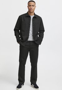 Black button-up shirt with two chest pockets, gray crew-neck t-shirt underneath, paired with black trousers and navy sneakers with white stripes.