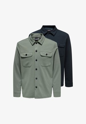 Twee overhemden met lange mouwen en knopen, met kraag en borstzakken met knopen; één in olijfgroen vooraan, één zwart erachter op een witte achtergrond.