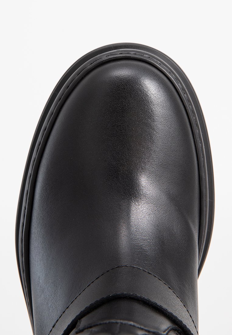 Schwarzer Lederschuh mit abgerundetem Zeh, glatter Textur, kontrastierenden Nähten und leichtem Glanz. Er verfügt über eine Gummisohle und subtile Designelemente.