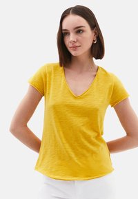 T-shirt jaune à manches courtes avec un col en V et une coupe décontractée. Texture douce, motif de stries subtil et ourlet incurvé.