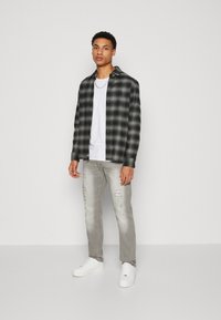 Black and grey plaid flannel shirt buttoned over a white t-shirt, paired with light distressed jeans and white sneakers.