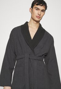 Szary bathrobe wykonany z węgla drzewnego z kontrastowym czarnym kołnierzem szalowym, paskiem wiązanym i dwoma przednimi kieszeniami. Teksturowana tkanina z długimi rękawami.