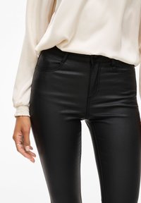 Svart faux läder högmidjade byxor med en smal passform, med framfickor och subtila stygn detaljer. Matchas med en flödande krämfärgad topp.