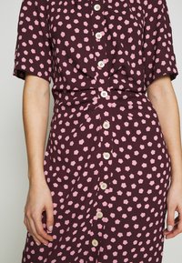 Kurzärmliges Kleid aus burgunderfarbenem Stoff mit einem pinken Blumenmuster, ausgestattet mit einer Knopfleiste vorne und Taillendetails für eine figurbetonte Silhouette.