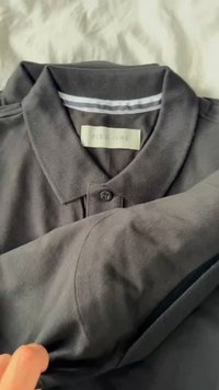 Tricou polo gri închis din bumbac, cu un închidere cu butoane, guler și o etichetă pe care scrie "PIER ONE." Material texturat și finisaj neted.