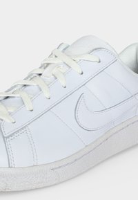 Λευκό αθλητικό παπούτσι Nike με κλεισίματος κορδονιών, υφασμένο πέλμα και ραμμένο λογότυπο Nike swoosh στο πλάι.