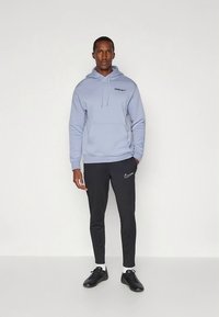 Vaaleansininen huppari, jossa on kiristysnauhat ja teksti "SPURS". Mustat vetoketjuhousut, joissa pieni valkoinen Nike-swoosh, yhdistettynä mustiin urheilukenkiin.