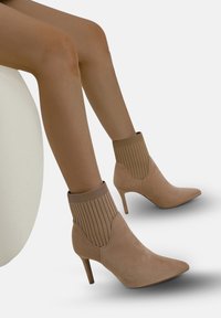 Stivali alla caviglia beige con punta affusolata e tacco alto, dotati di una parte superiore a forma di calza caratterizzata da un materiale testurizzato con riga.