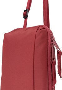 Borsa in nylon rosso con forma rettangolare piatta, dotata di chiusura con zip e tracolla regolabile. La superficie presenta una finitura testurizzata, con piccoli dettagli hardware.