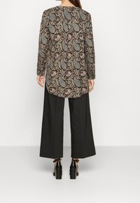 Blusa de manga larga en negro con un estampado de paisley en tonos verde azulado y rosa. Combinada con pantalones anchos negros y zapatos de tacón grueso.