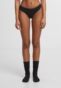 Svarte hipster undertøy laget av myk stoff med en glatt tekstur. Kombinert med knelange svarte sokker med en rynket design.