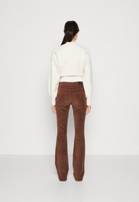 Bruine corduroy flare broeken met achterzakken, gecombineerd met een crèmekleurige cropped sweater. Glad textuur met geribde boorden, zonder zichtbare logo's.