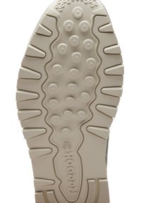 Semelle de chaussure avec motifs de bande de roulement circulaires et linéaires, couleur beige, avec logo Reebok et motif en étoile près de la zone du talon.