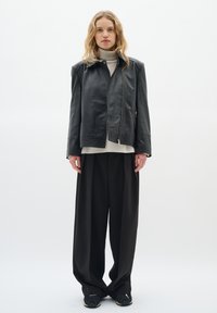 Jachetă din piele neagră cu închidere prin fermoar, croială lejeră și design minimalist. Asortată cu pantaloni negri largi și un pulover bej cu guler înalt.