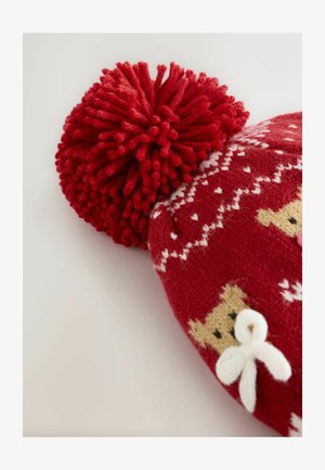 Bonnet en tricot rouge avec un grand pompon rouge, des motifs de cœurs blancs et des visages d'ours avec des nœuds blancs. Texture douce et design festif.