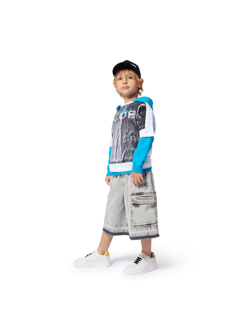 Huvtröja i grått och turkos, kombinerad med ljusgrå cargoshorts med en sidoficka; vita sneakers med gula accenter.