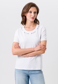 White short-sleeve t-shirt featuring metallic silver loop accents near the neckline, made from soft cotton fabric, with a relaxed fit.