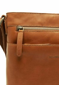 Brown leather crossbody bag featuring a front zip pocket, visible stitching, and a soft texture. Adjustable strap for versatile carrying.