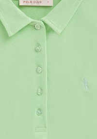 Ljusgrön polo av texturerad tyg, med knappslå, tre knappar och en liten vit broderad logotyp.