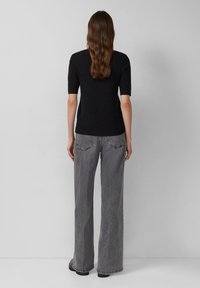 Zwart gebreid top met korte mouwen, gecombineerd met hoogsluitende, wijde grijze jeans. Getextureerde stof en rafelige zoomdetails op de jeans.