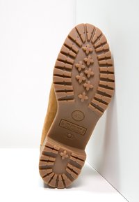 Ruskea kumi-pohja, jossa on jäykkä kuvio, joka sisältää Timberland-logon. Yläosa on tehty vaaleasta mokkanahasta.