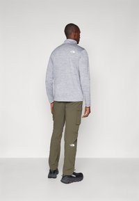 Siva flis jakna s visokim ovratnikom, uparena s maslinasto zelenim cargo hlačama. Logo The North Face vidljiv je na oba odjevna predmeta. Crne planinarske cipele.