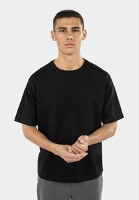 Svart T-skjorte med korte ermer laget av jersey-stoff, med rund halslinning og avslappet passform, brukt med grå bukser.