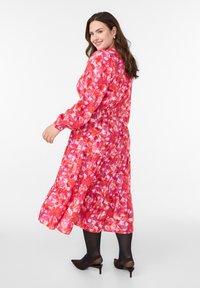 Gėlių modelio midi suknelė su susiraukšlėjusiu liemeniu, rožinėmis ir raudonomis atspalviais. Ilgos rankovės, pakopinė apatinė dalis, derinama su rudos spalvos smailiakulniais bateliais.