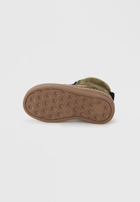 Botte en suède verte avec une semelle en caoutchouc texturé présentant un motif en nid d'abeille. Le talon est renforcé par un accent en tissu noir.