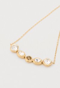 Auksinis karoliai, turintis penkis skaidrius kristalus įvairių formų, įskaitant ovalinius ir heksagoninius, su gėlių metalo detalėmis centre.