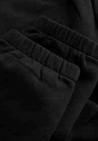 Musta puuvillakangas, jossa on kolme kerättyä kuminauha vyötäröllä, sileä pinta, hieman kiiltävä ja tasainen, yhtenäinen väri.