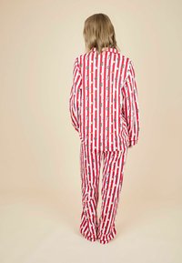 Rød- og hvidstribede pyjamas sæt med festlige mønstre, herunder kranse og julesokker, med en rummelig pasform og blød tekstur.