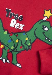 Tessuto rosso con un dinosauro cartone animato, "Tree Rex," avvolto in luci di Natale colorate, con una stella gialla sopra la testa.