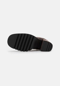 Suela de goma negra con surcos de tracción prominentes. La parte superior presenta un suave material de ante marrón, mostrando un diseño texturizado y tonal.
