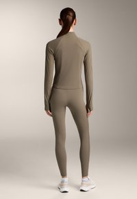 Sportstøj med en tætsiddende langærmet top og matchende leggings, begge i lys olivengrøn ribbet stof, med strømlinet design.