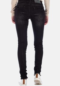 Jeans neri skinny con una texture sbiadita, vita media, due tasche posteriori e orlo grezzo corto, abbinati a sneakers bianche con un accento marrone.