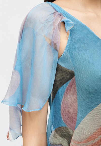 Κοντινή λήψη μπλε φορέματος με διάφανα, αέρινα κοντά μανίκια και αφηρημένα πολύχρωμα μοτίβα στο ύφασμα.