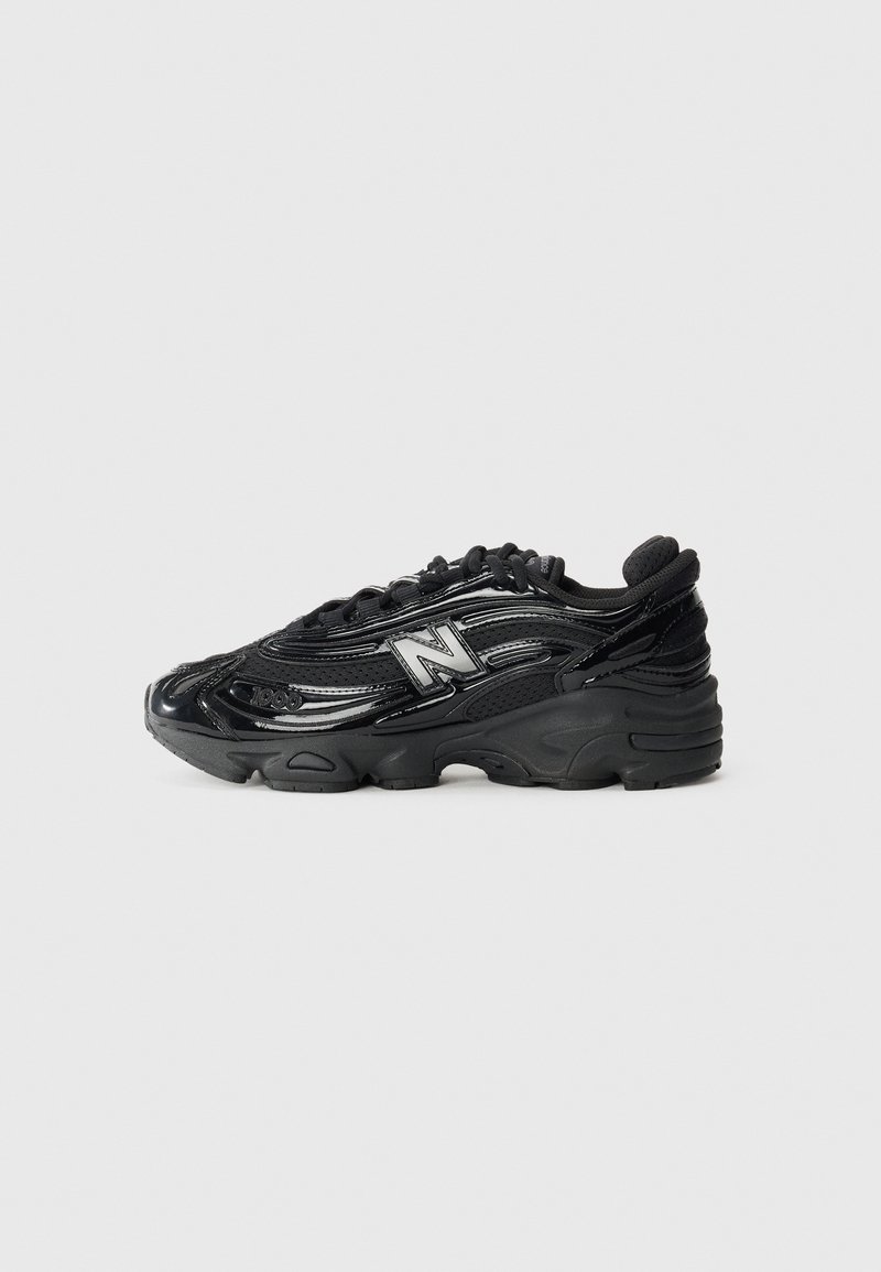 Baskets noires New Balance avec des détails brillants, logo "N" sur le côté, semelle épaisse et fermeture à lacets, montrées de profil sur fond clair.