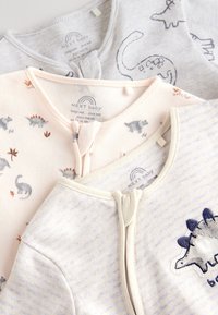 Trois ensembles pour bébé : gris clair avec imprimé dinosaure, rose clair avec motifs d'animaux, et crème rayé avec un appliqué dinosaure. Texture en coton doux.