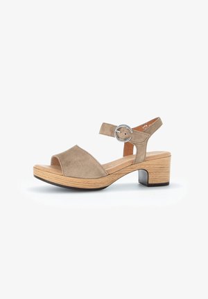Beige suede heeled sandals with an open toe, slingback strap and circular silver hardware, featuring a textured wooden block heel.